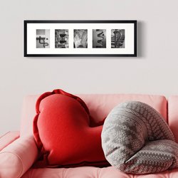 4EVER - für immer, zusammengesetzt aus fünf Alphabet Fotos in Schwarz-Weiß. Umrandet mit einem weißen Passepartout und gerahmt in einen schwarzen Bilderrahmen. Das Bild hängt an der Wand über einem rosa Sofa, auf dem sich ein rotes Kissen in Herzform und ein graues Kissen befindet.arunter 