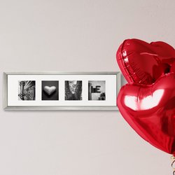 Liebesgeschenk LOVE, zusammengsetzt aus vier schwarz-weißen Alphabet Fotos. Diese sind mit einem weißen Passepartout umrandet nd in einem grauen Bilderrahmen aus Holz an der Wand angebracht. An der rechten Seite befinden sich zwei rote Folienballons in Herzform.